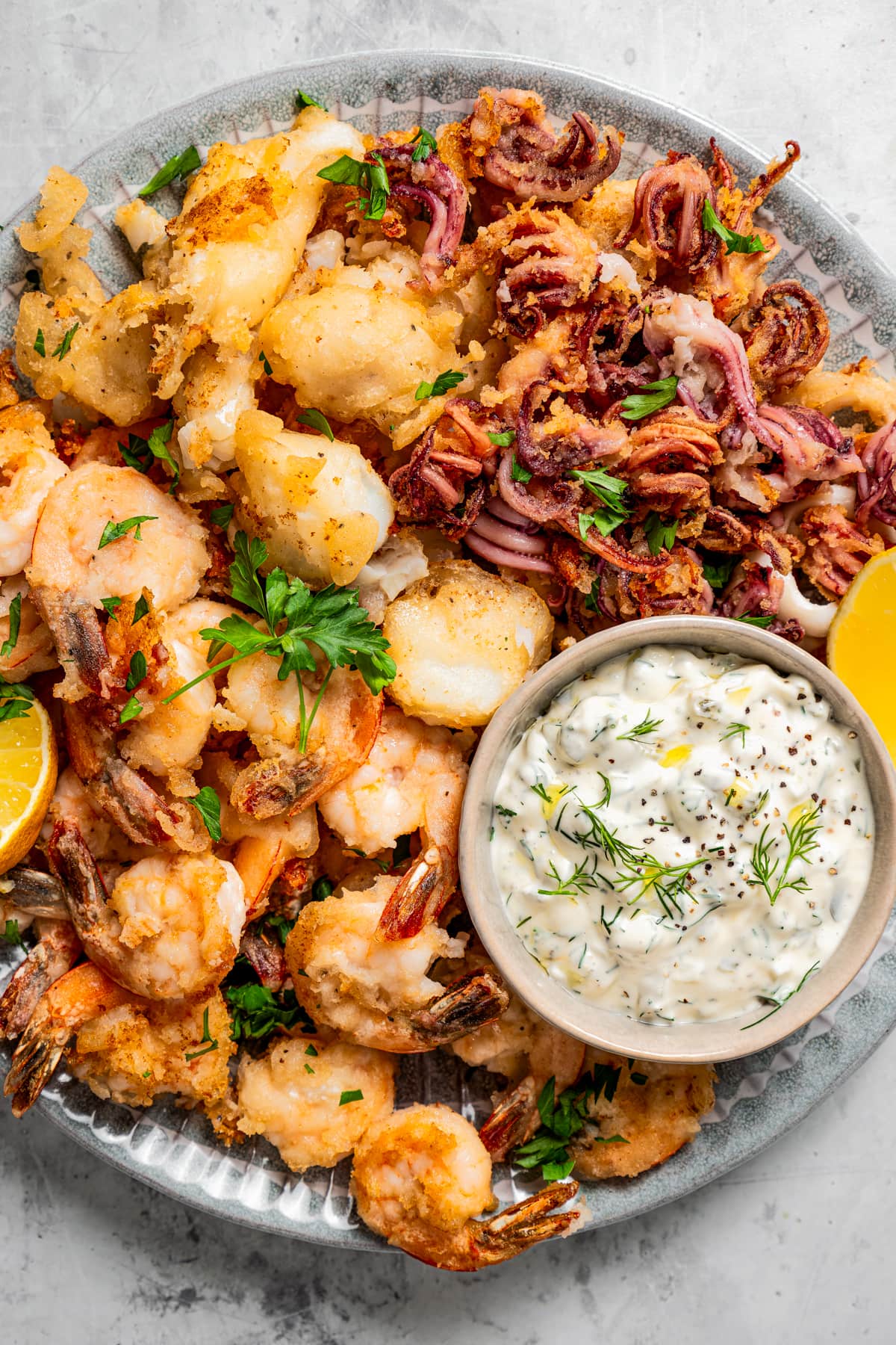 A round plate filled with battered and fried shrimp, cod, and calamari, with a tartar sauce served in a bowl.