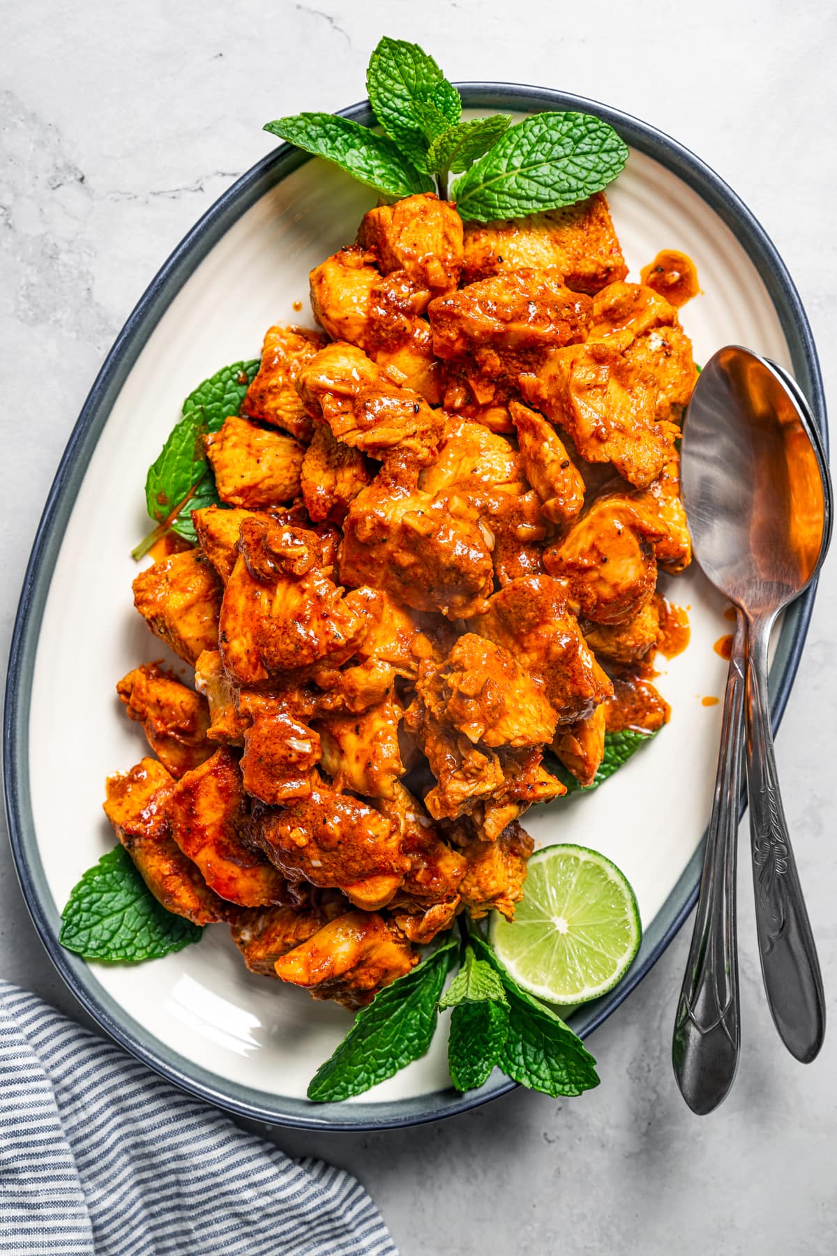 Chicken bites tossed with harissa paste mixture and served on an oval platter, garnished with lime and green herbs.