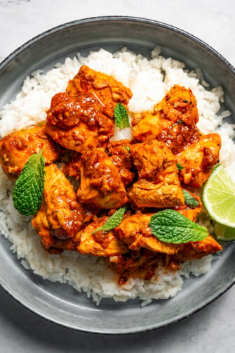 Harissa chicken served over rice and garnished with fresh green herbs and lime wedges.