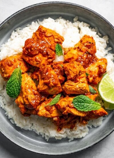 Harissa chicken served over rice and garnished with fresh green herbs and lime wedges.