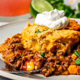 A slice of tamale pie on a plate with a dollop of sour cream on top.