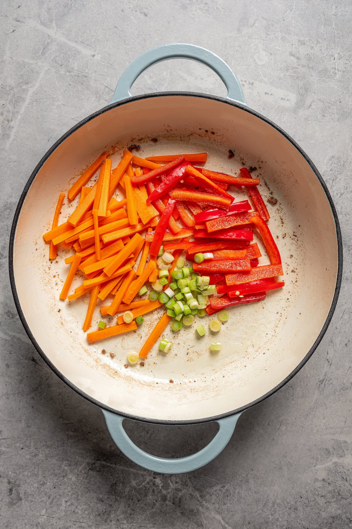Julienne carrots and red bell peppers added to a skillet with scallions.