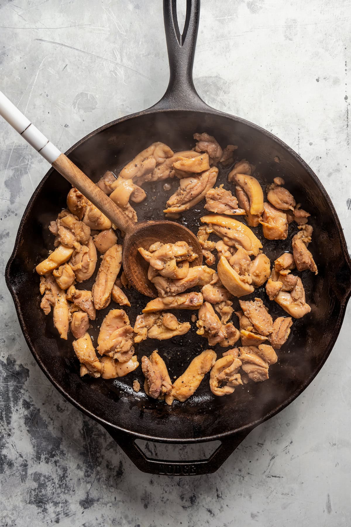 Sauteed chicken pieces in a skillet with a wooden spoon.