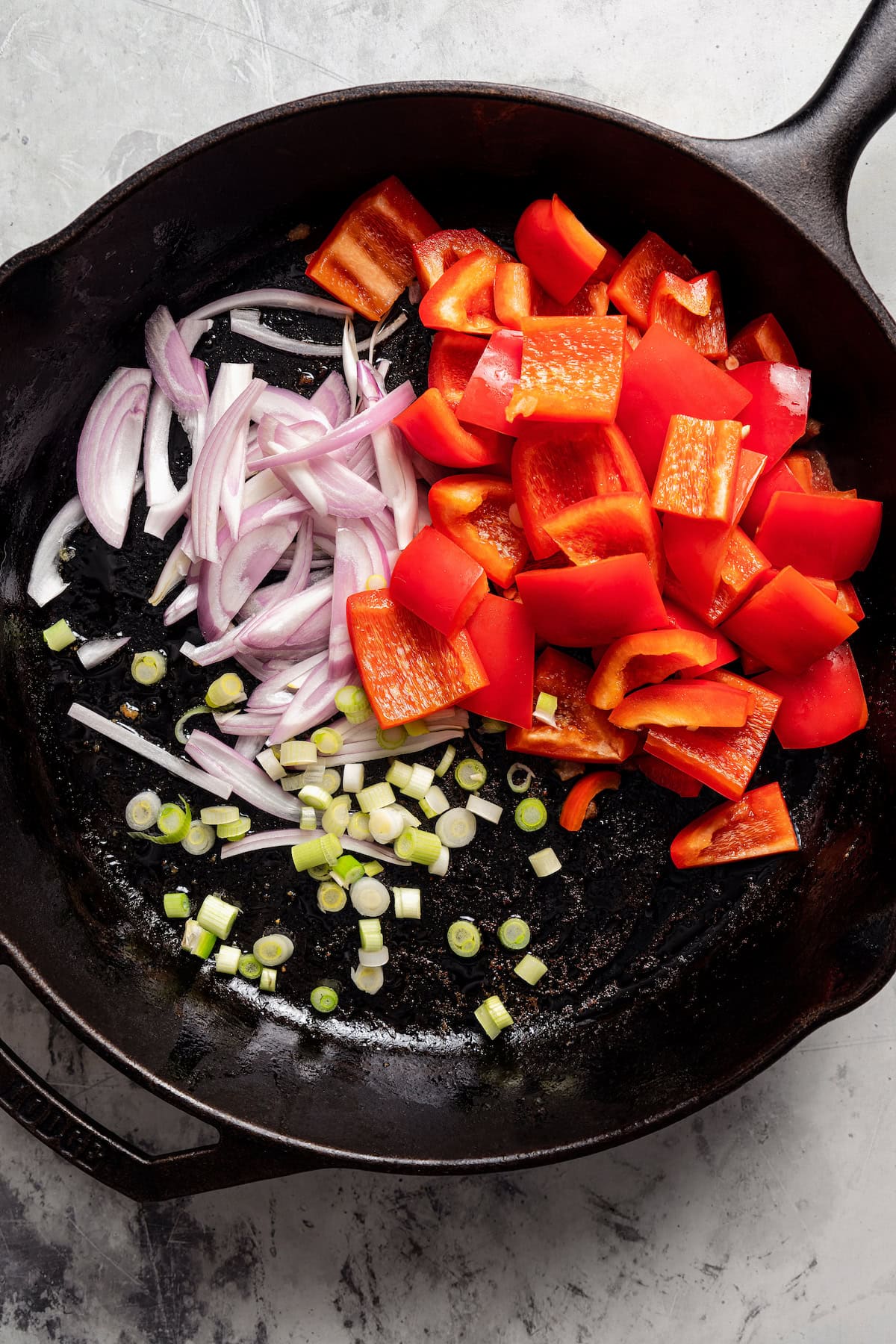 Red bell peppers, scallions, and onion combined in a skillet.