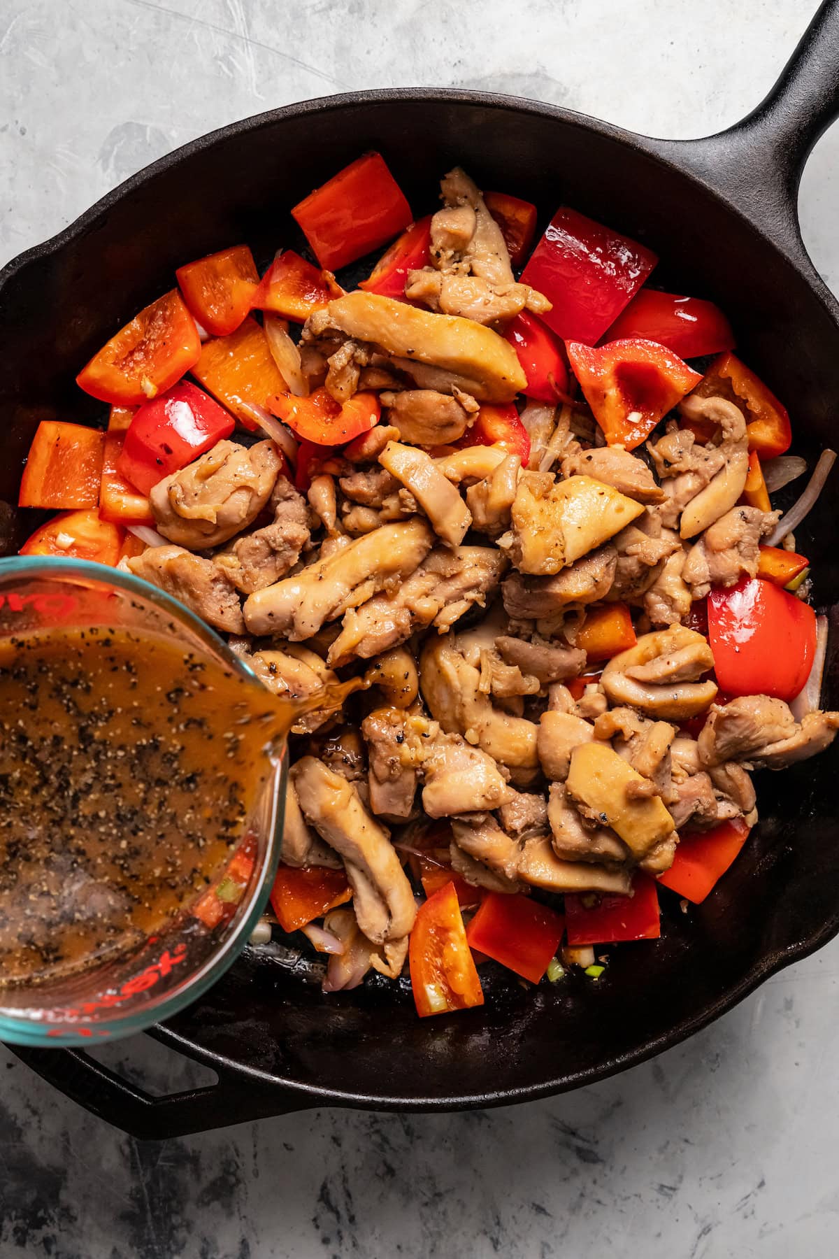 Black pepper marinade being poured over sauteed chicken and bell peppers in a skillet.