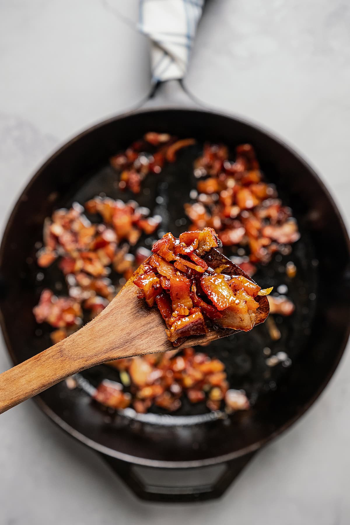 Close up of bacon jam on a wooden spoon, held over a black skillet.