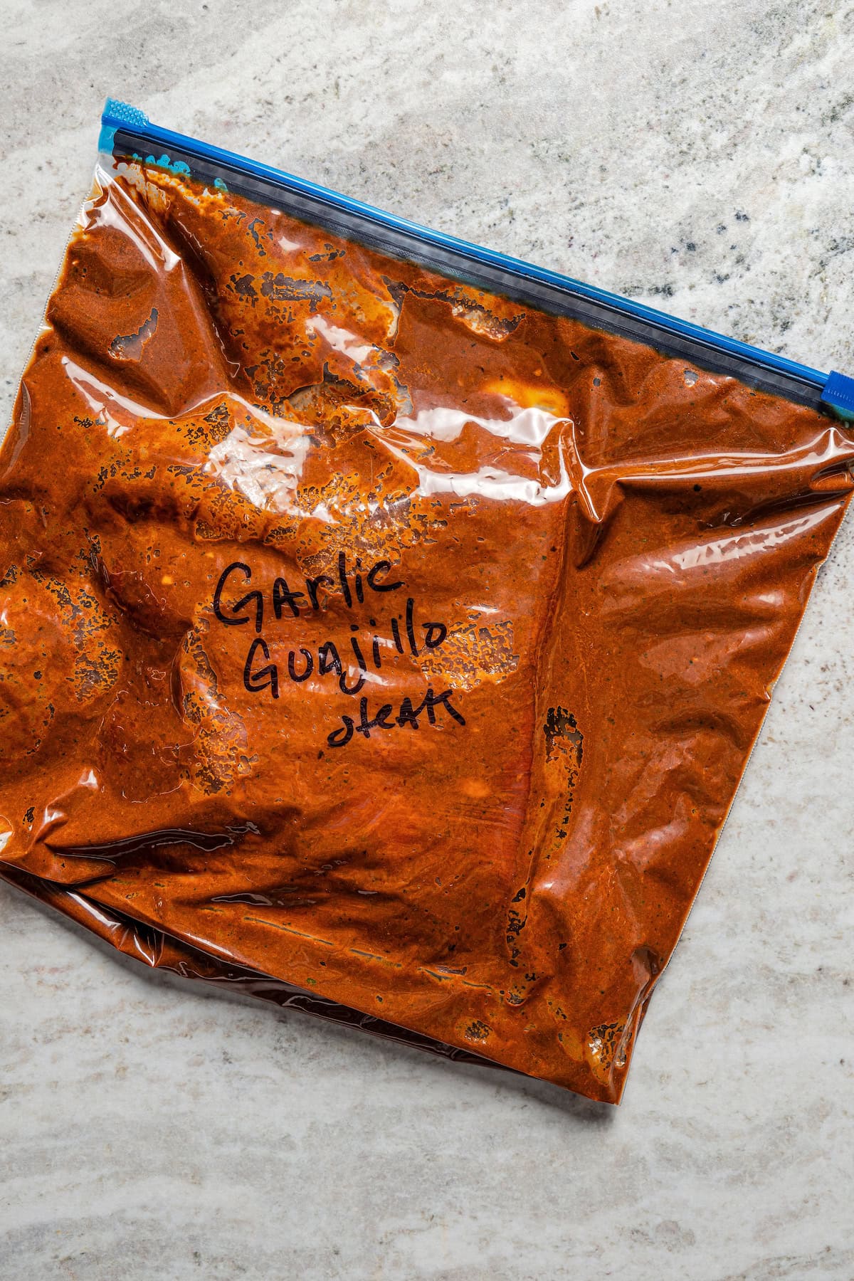 A labeled ziploc bag containing steak soaking in garlic guajillo marinade.