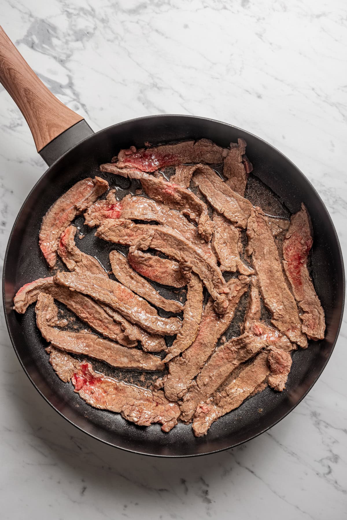 Browned beef strips in a skillet.