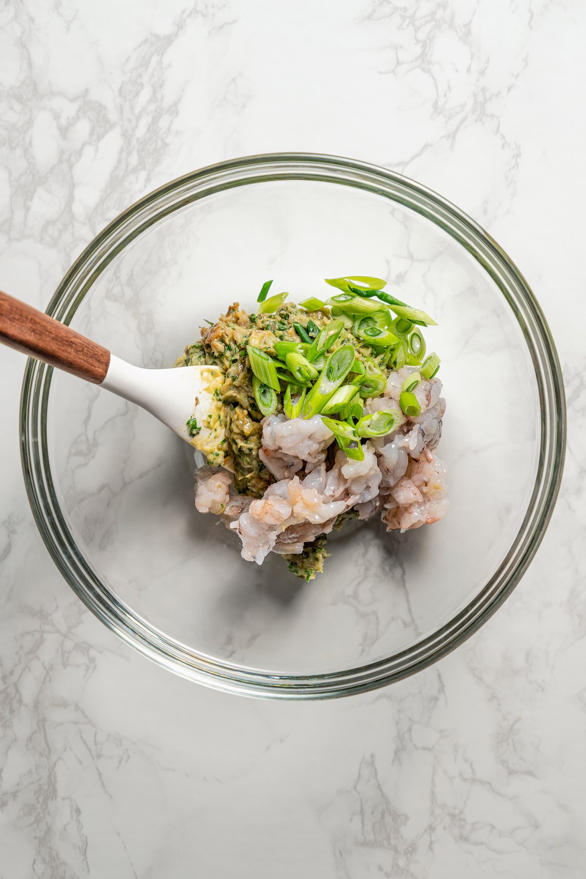 Shrimp shumai filling ingredients combined in a glass bowl with spatula.