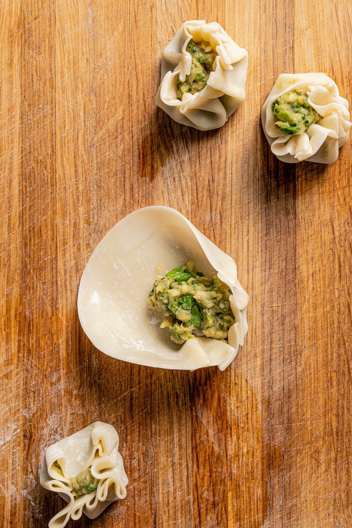 A dumpling wrapper partially folded around shrimp shumai filling on a wooden board.