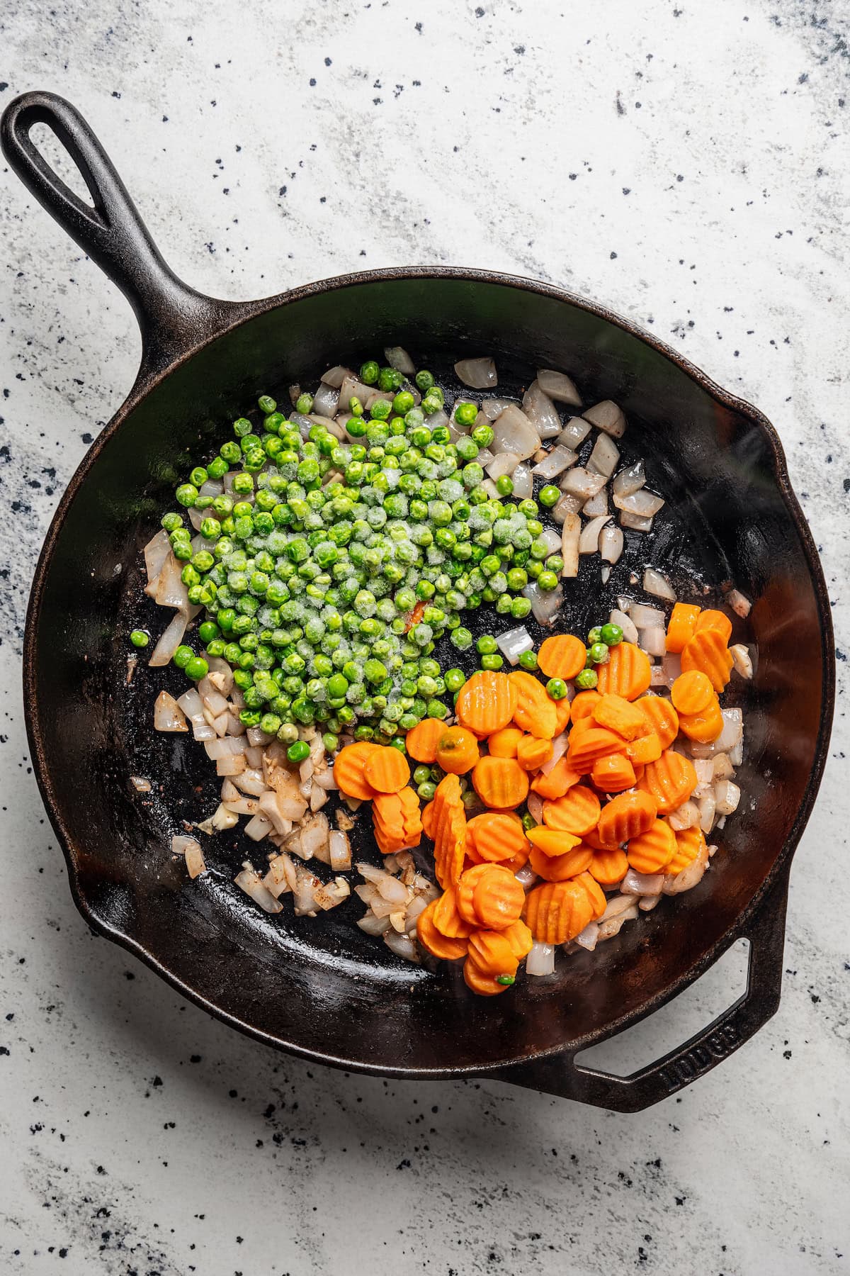 Onions, frozen peas, and carrots added to a skillet.