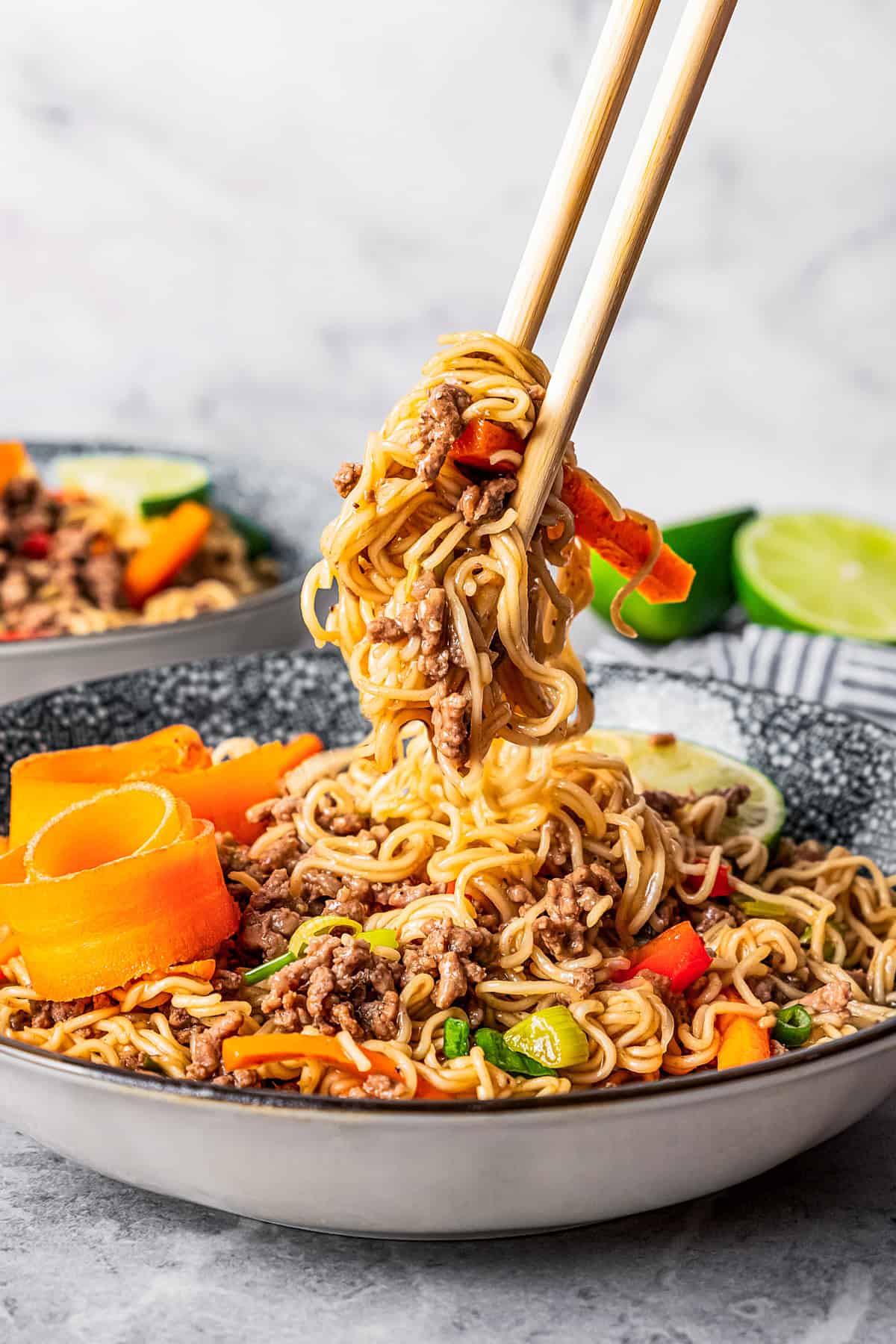 Chopsticks lifting beef ramen noodles from a bowl.
