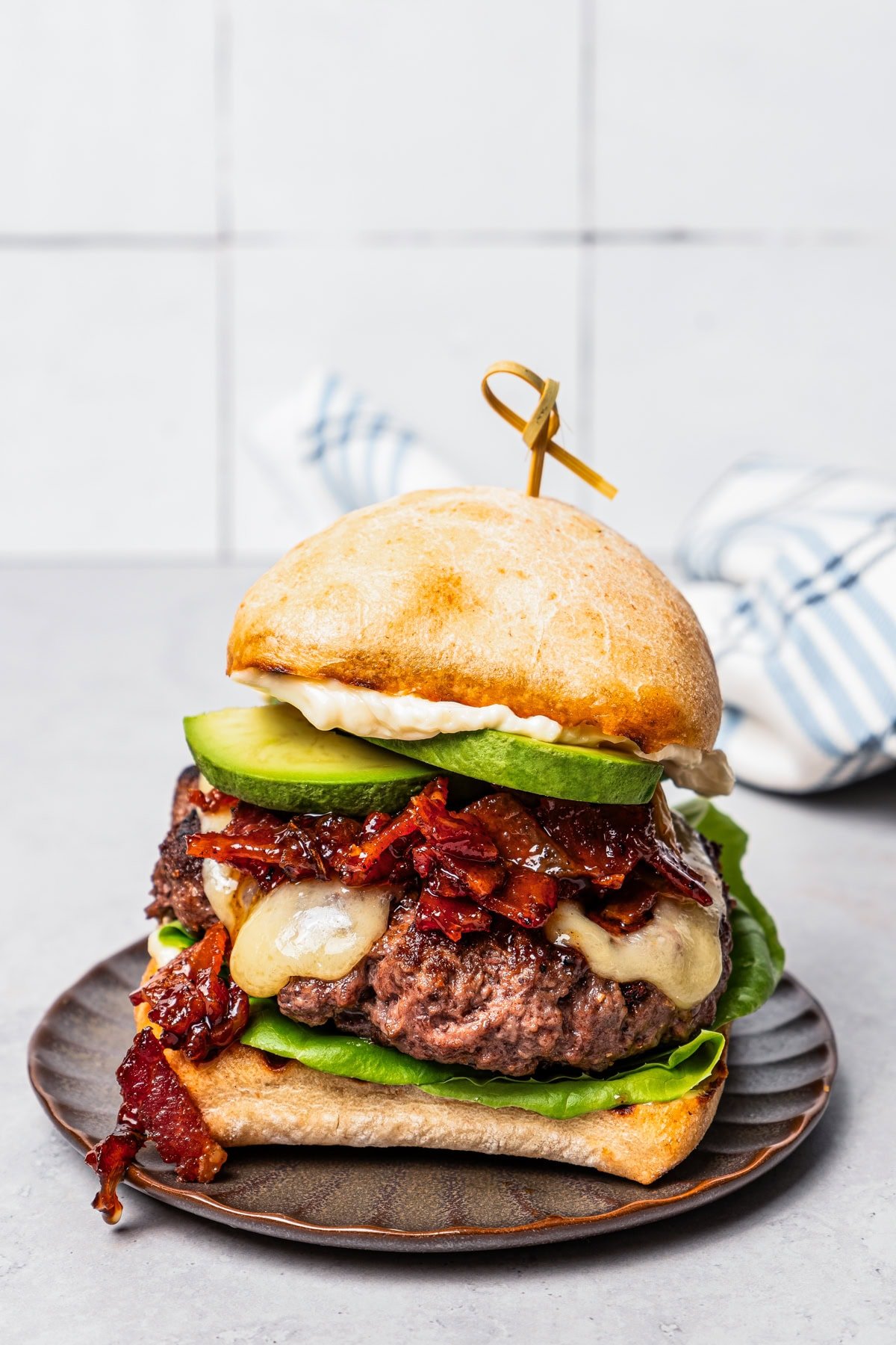 Burger with beef patty, avocado slices, and bacon jam served on a brown plate.