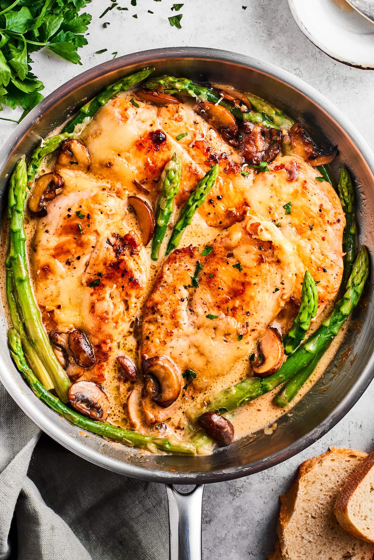 A skillet with a few cooked chicken breasts and asparagus stalks.
