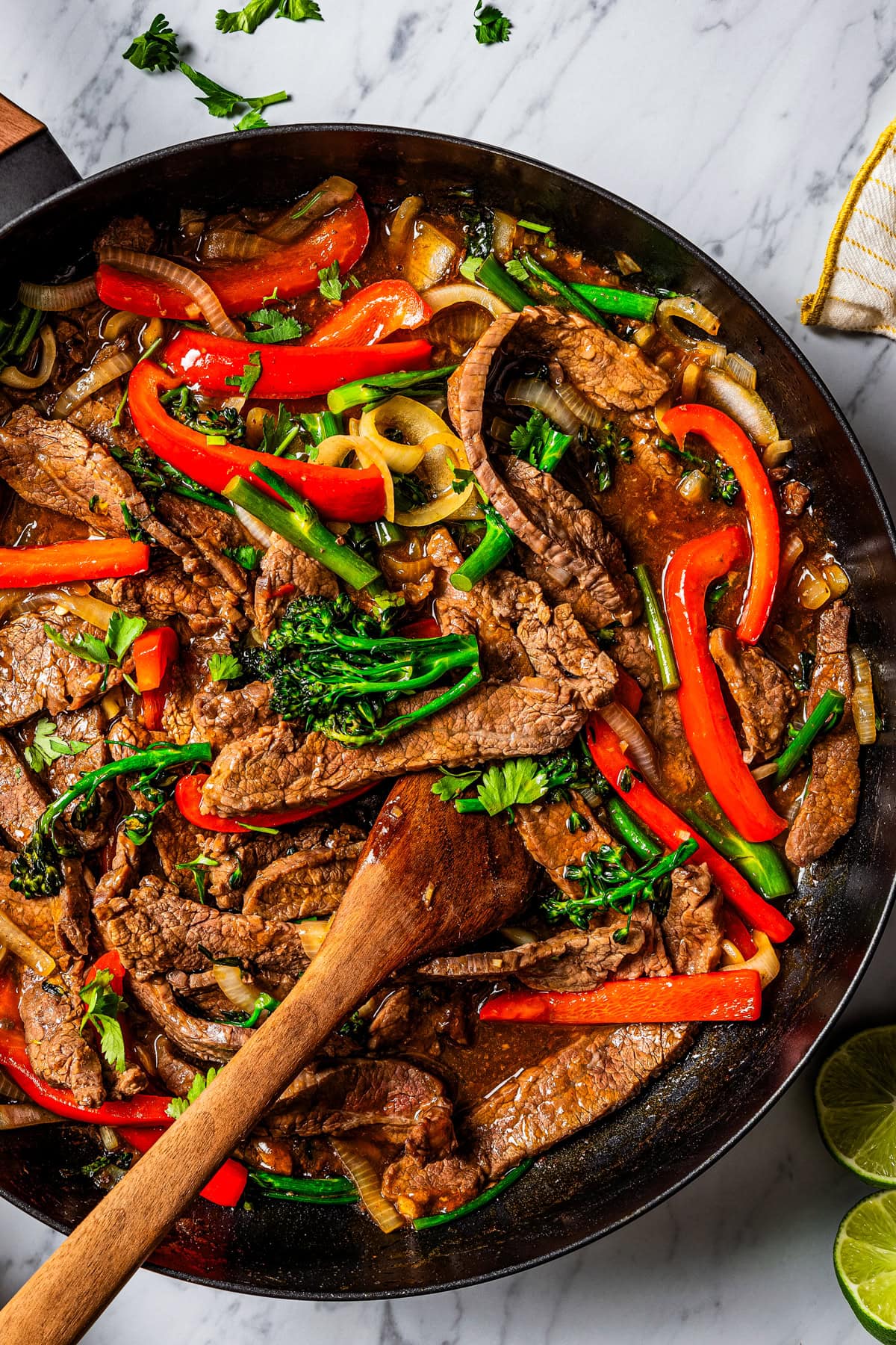 Image of Hunan beef in a skillet with a wooden spoon stirring through it.