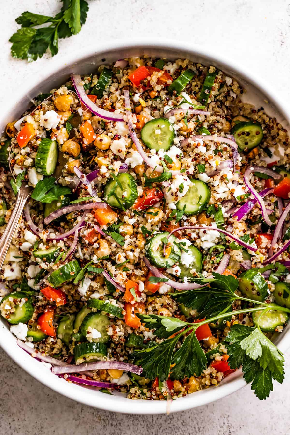 Salad bowl with quinoa, sliced cucumbers, sliced red onions, chickpeas, peppers, and nuts.
