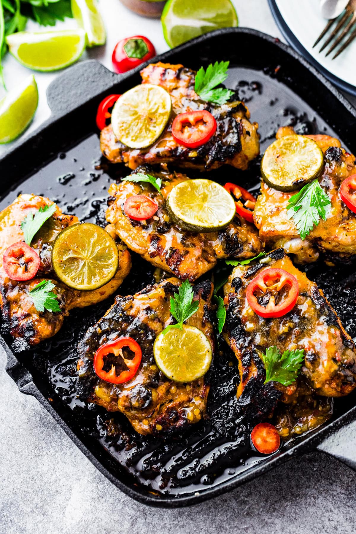 Lemongrass chicken on a grill pan with lime slices and chilis.