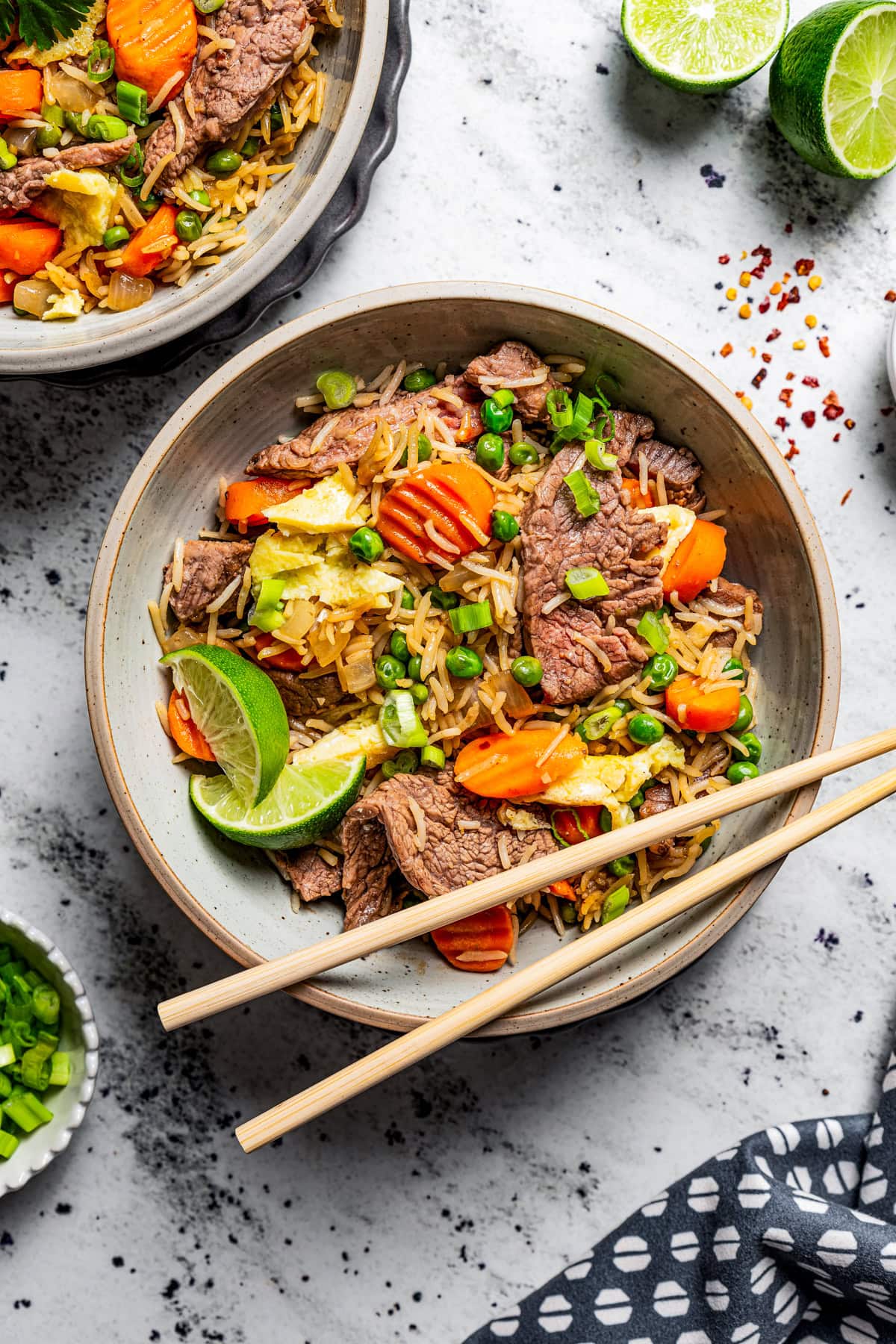 Steak fried rice served in two bowls with chopsticks resting on one and lime wedges positioned nearby.