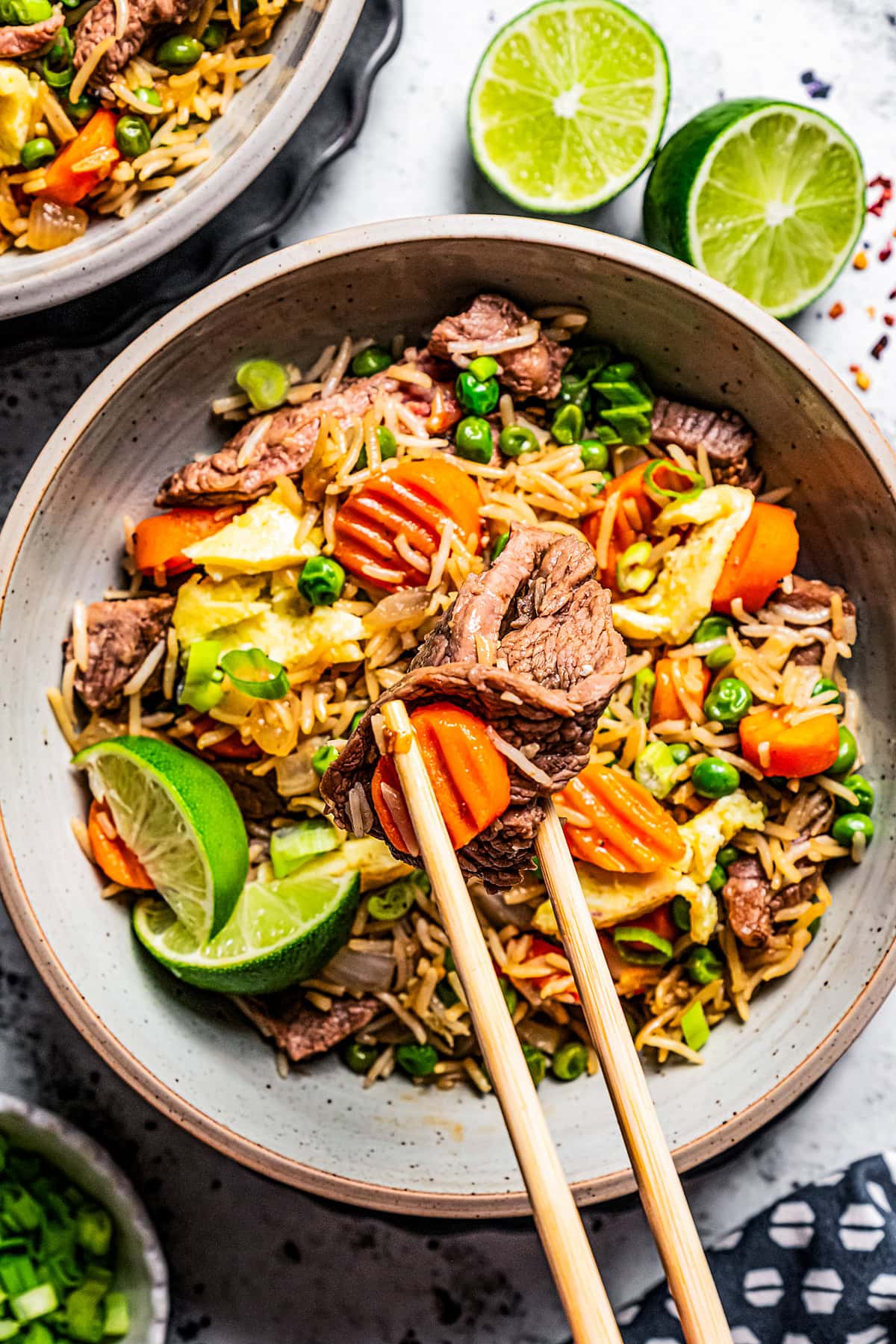 Chopsticks reaching for a strip of steak in a bowl filled with rice, beef, carrots, and eggs.