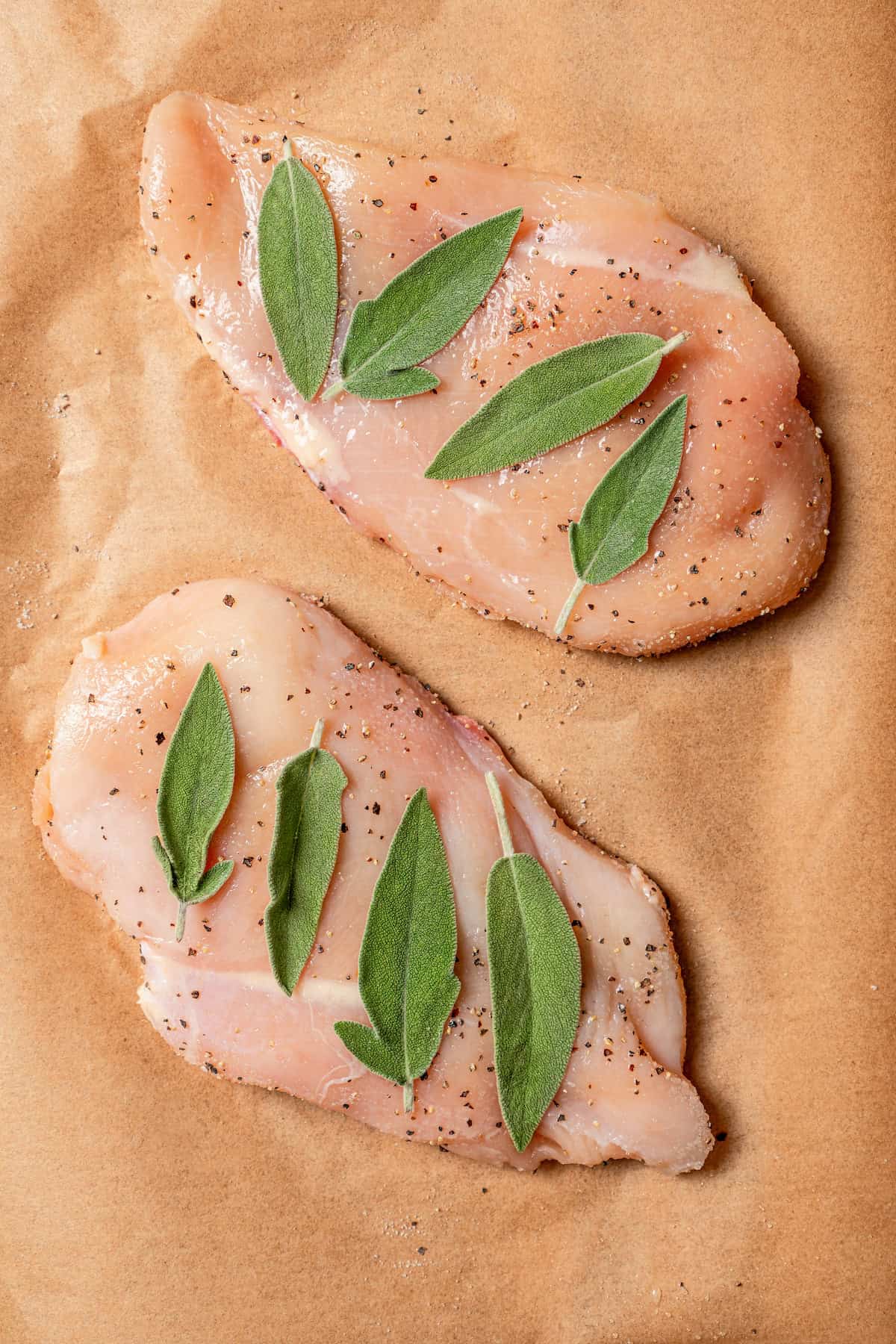 Chicken breasts topped with sage leaves on a piece of parchment paper.