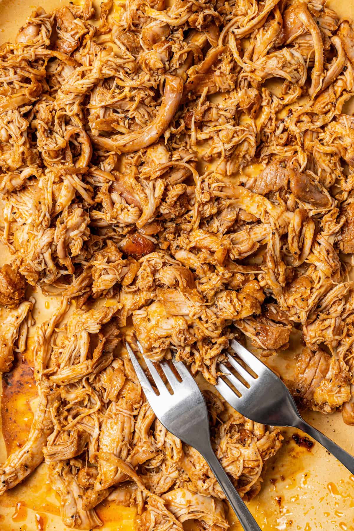 Shredded chicken on a wooden cutting board with two forks.
