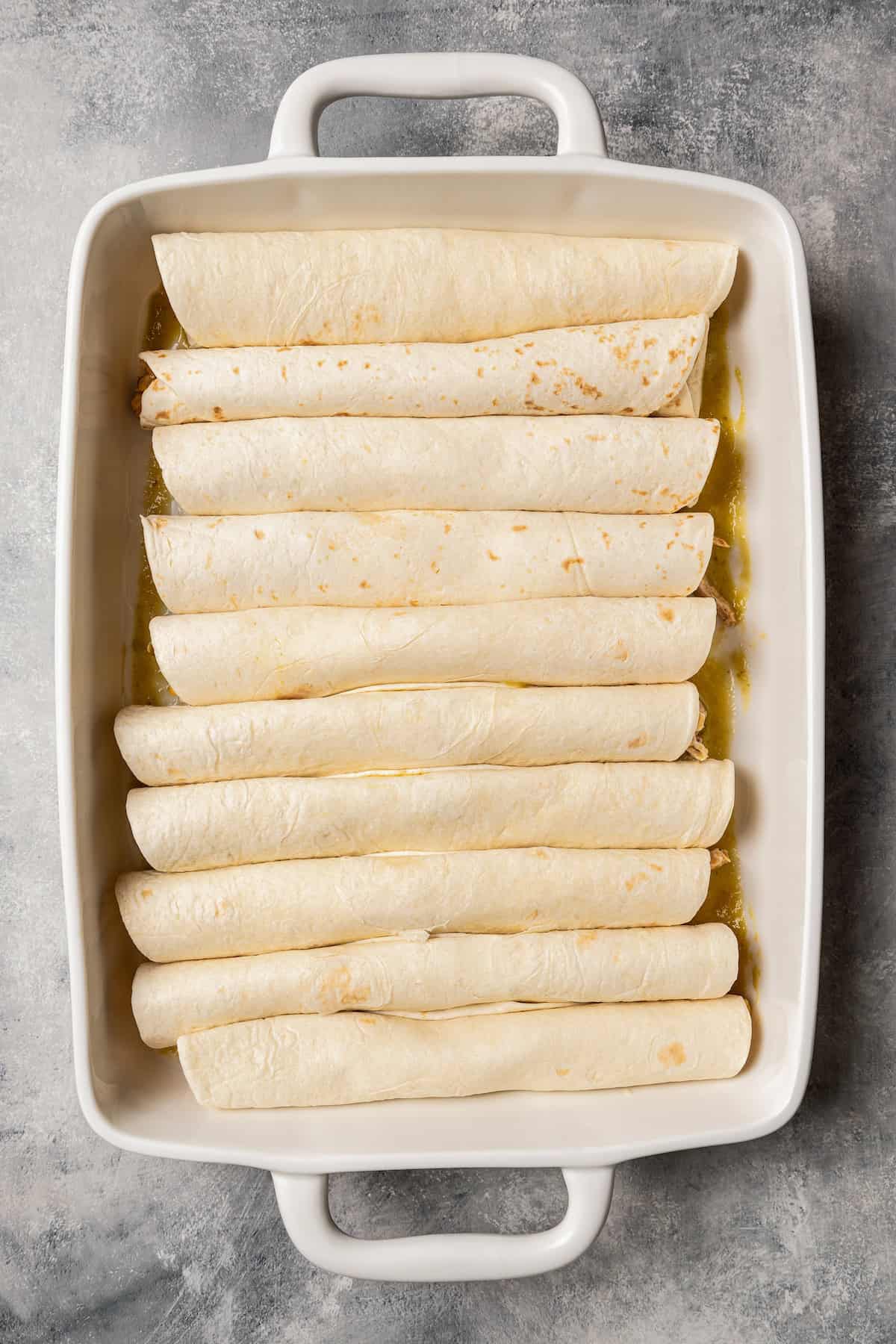 Filled and rolled flour tortillas lined up inside a baking dish.