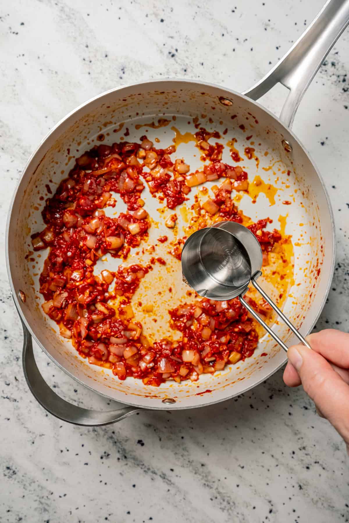 A spoonful of pasta water is added to onions sauteed in tomato paste in a skillet.