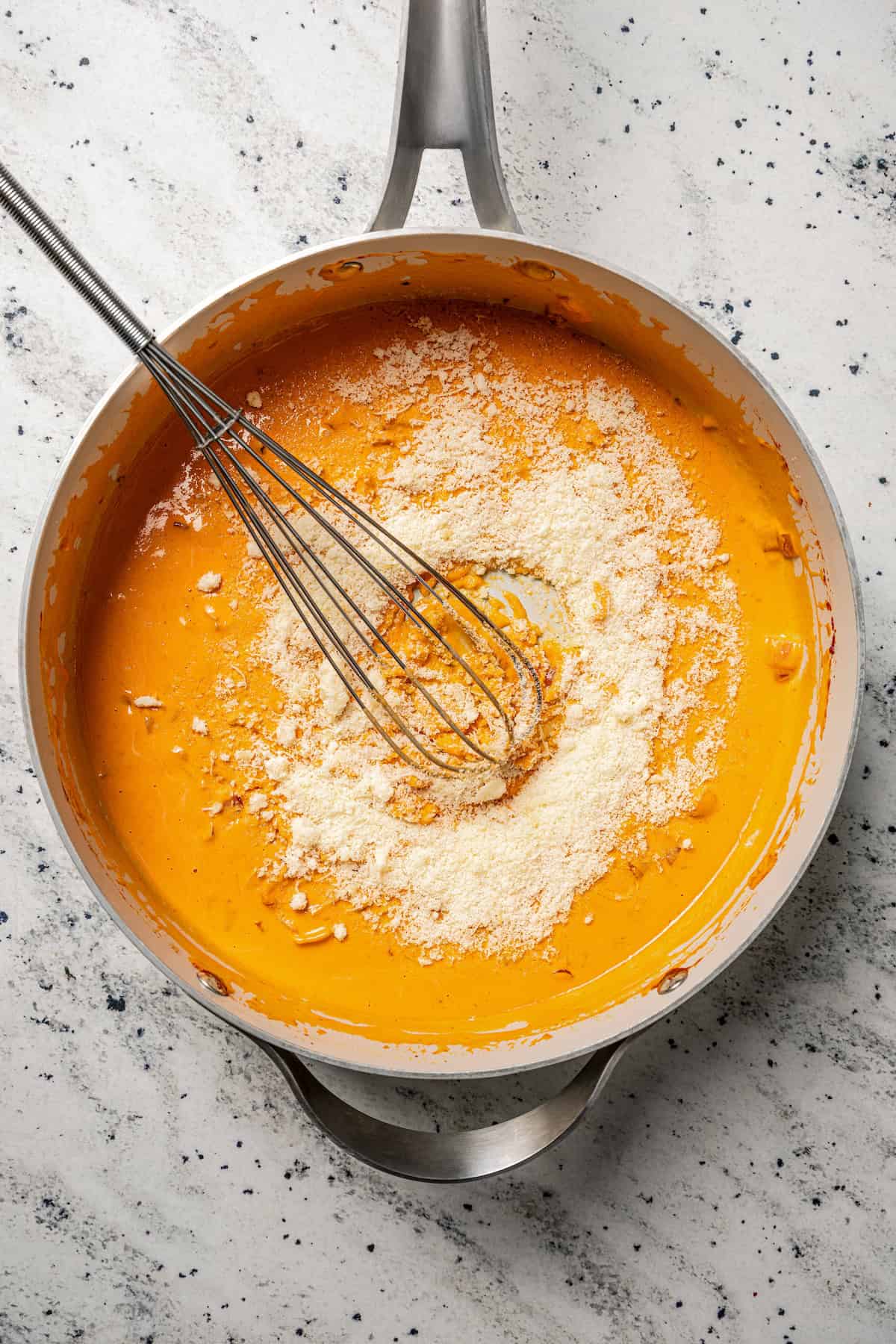 Grated parmesan cheese partially whisked into a skillet of vodka sauce.