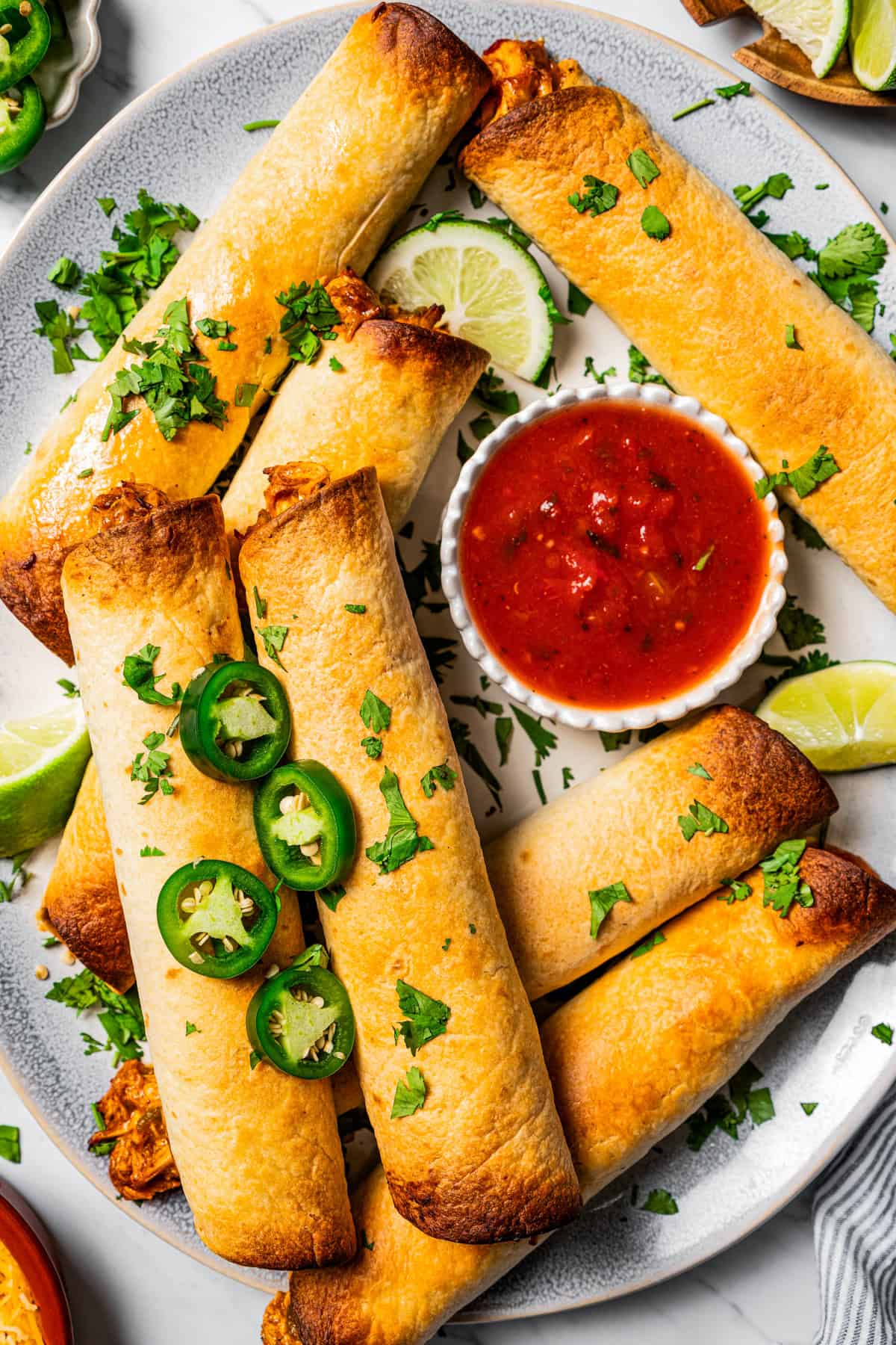 Chicken flautas arranged on a serving platter with a bowl of tomato salsa.