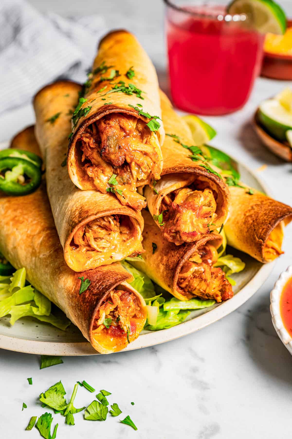 Six chicken flautas stacked over a bed of shredded lettuce on a plate.