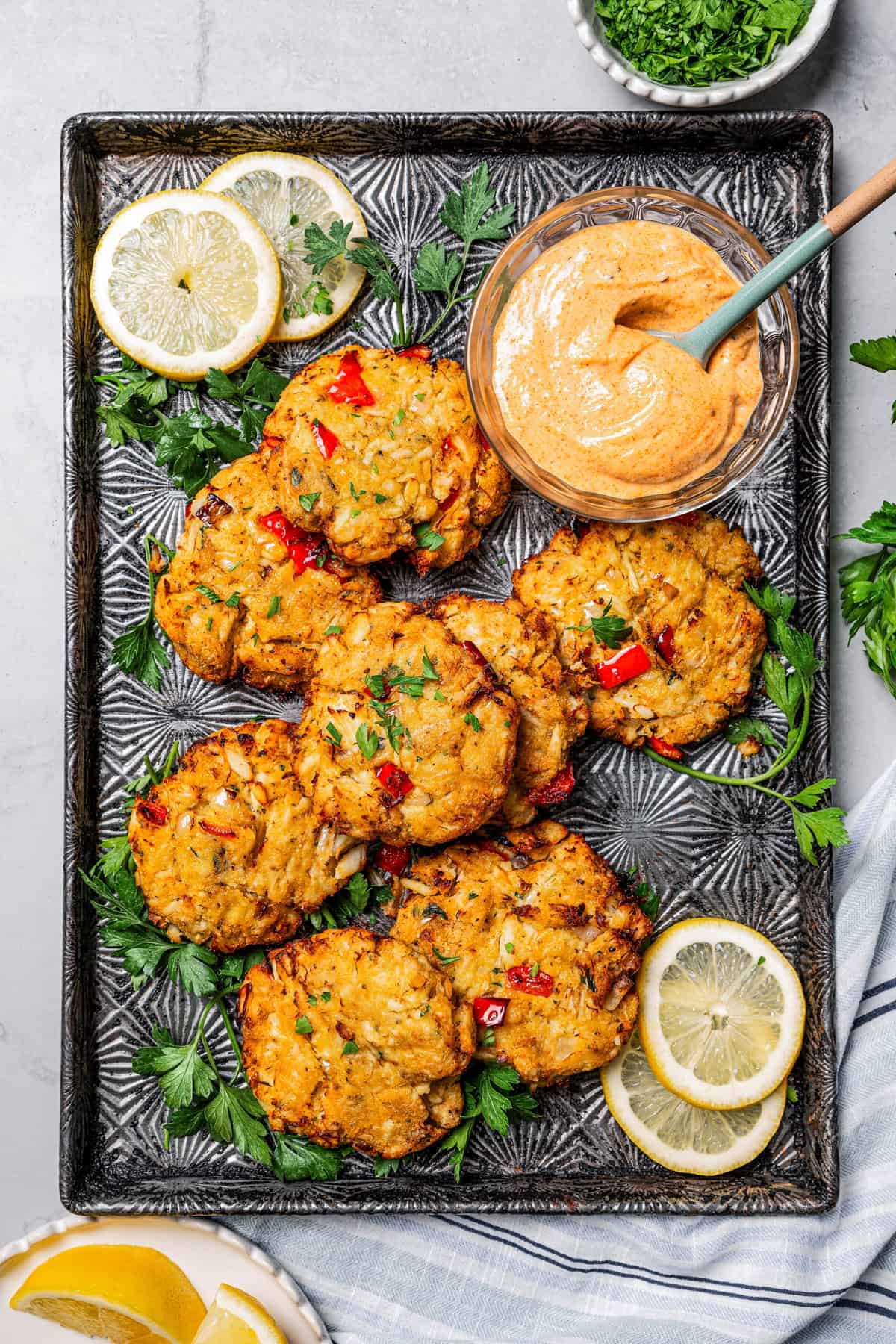 Overhead image of several crab cakes served on a tray with a bowl of remoulade to the side.