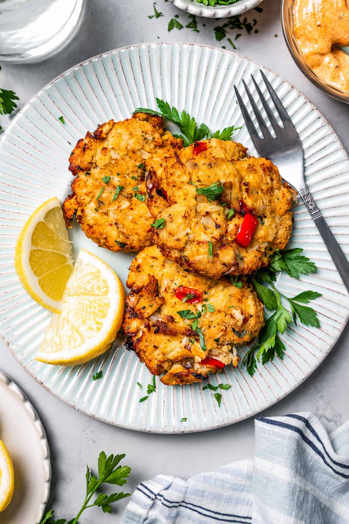 Air fried crab cakes served on a dinner plate and garnished with lemon wedges, next to a fork.