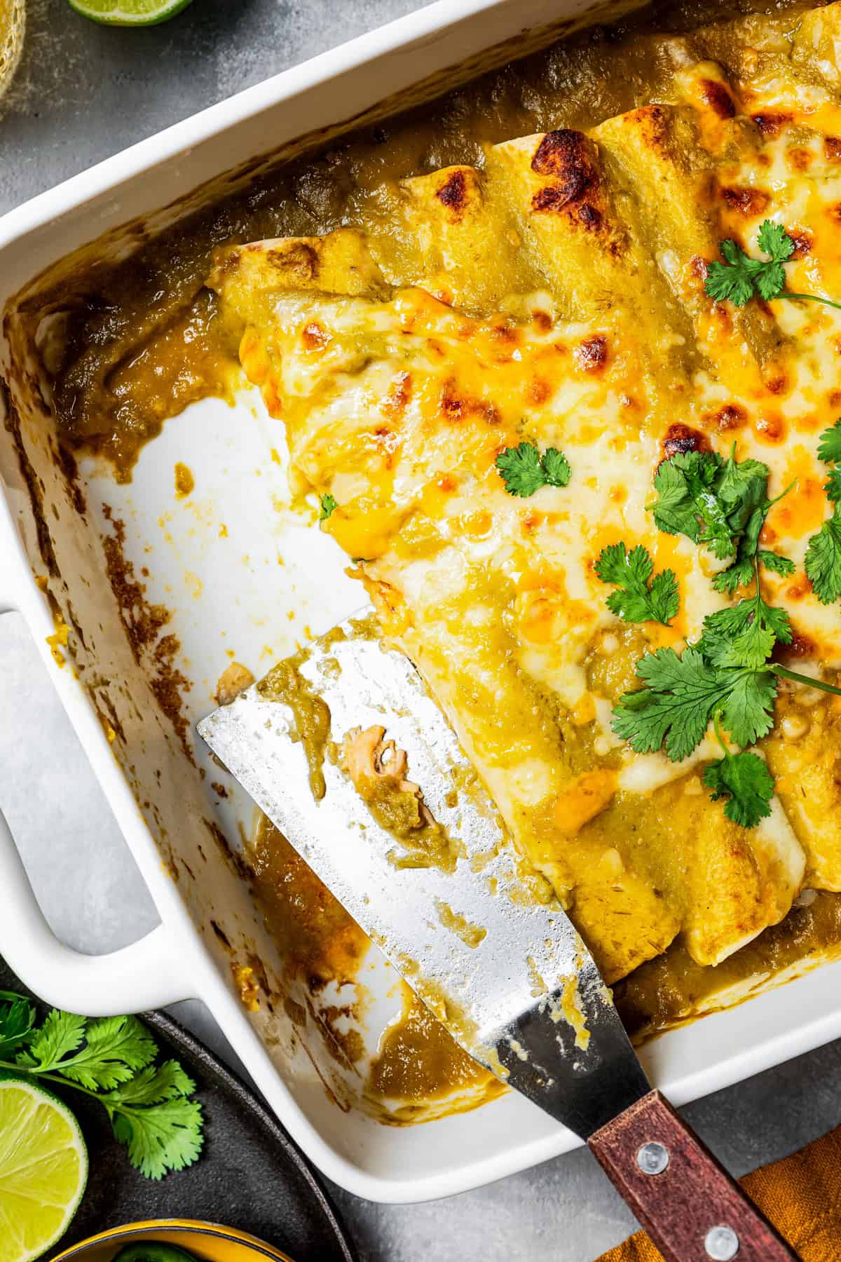 Overhead view of enchiladas in a baking dish with two portions missing, and a spatula resting in the dish.