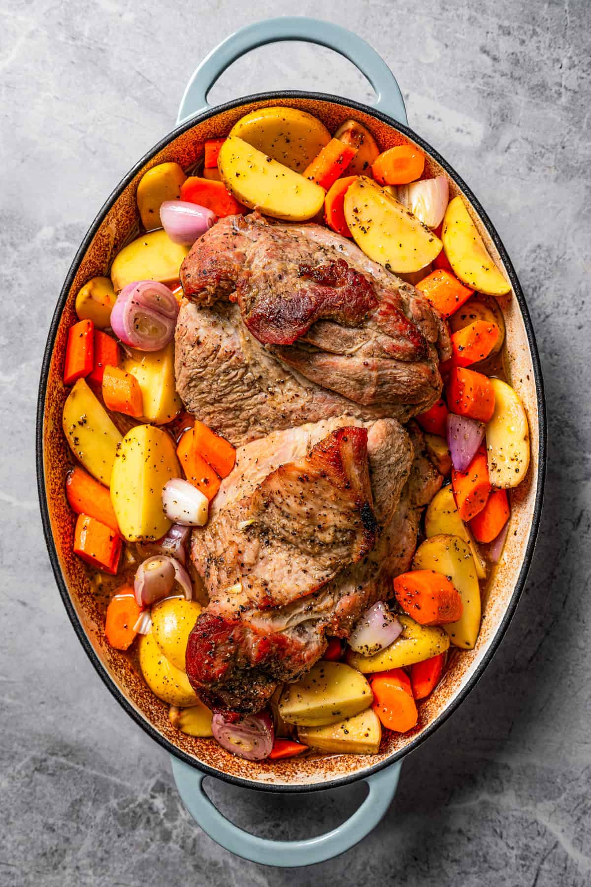 A whole pork roast surrounded by vegetables in an oval baking dish.