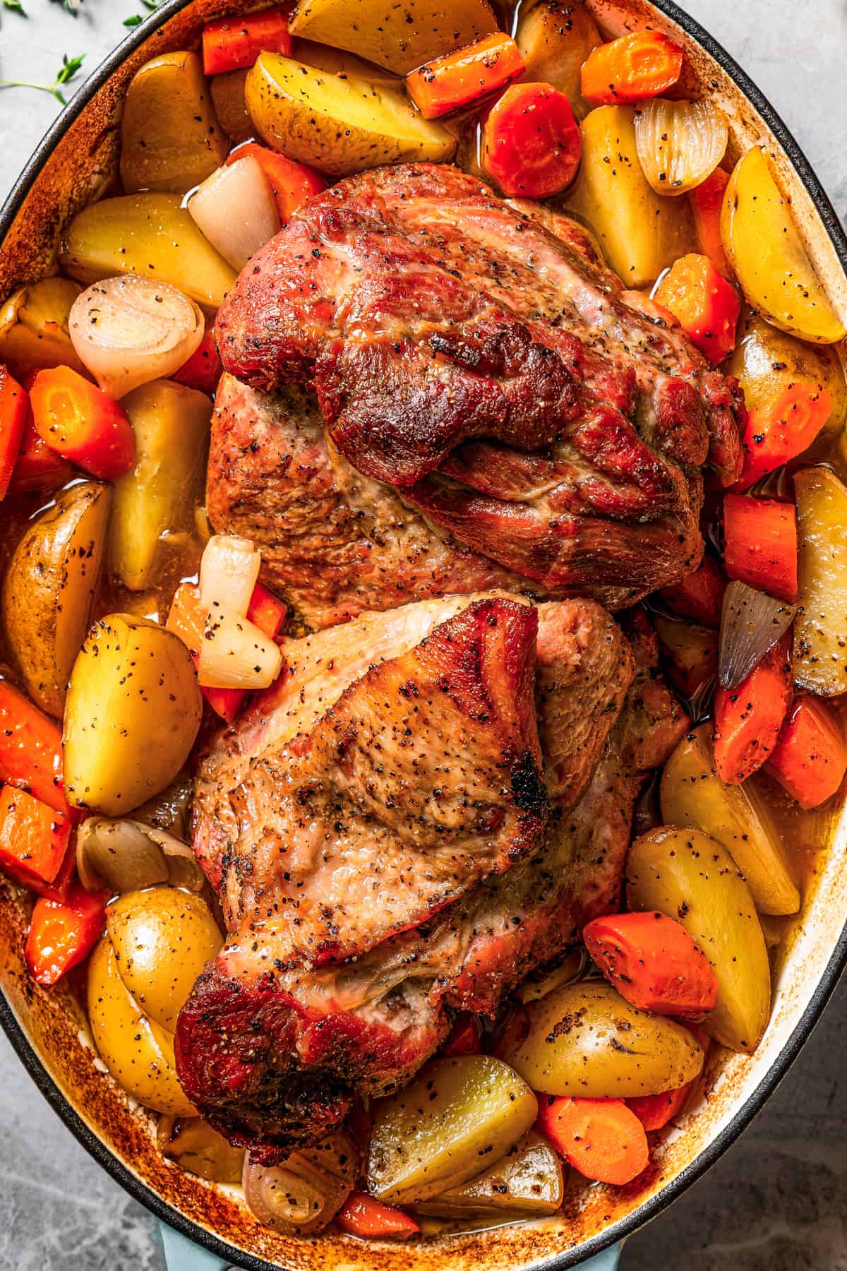 A pork roast surrounded by cut-up potatoes, carrots, and onions in a baking dish.