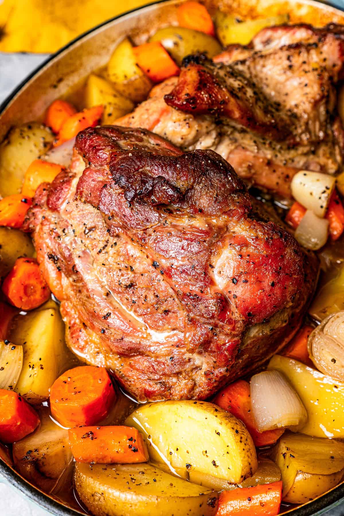 Close-up of a pork shoulder roast surrounded by roasted vegetables in a baking dish.