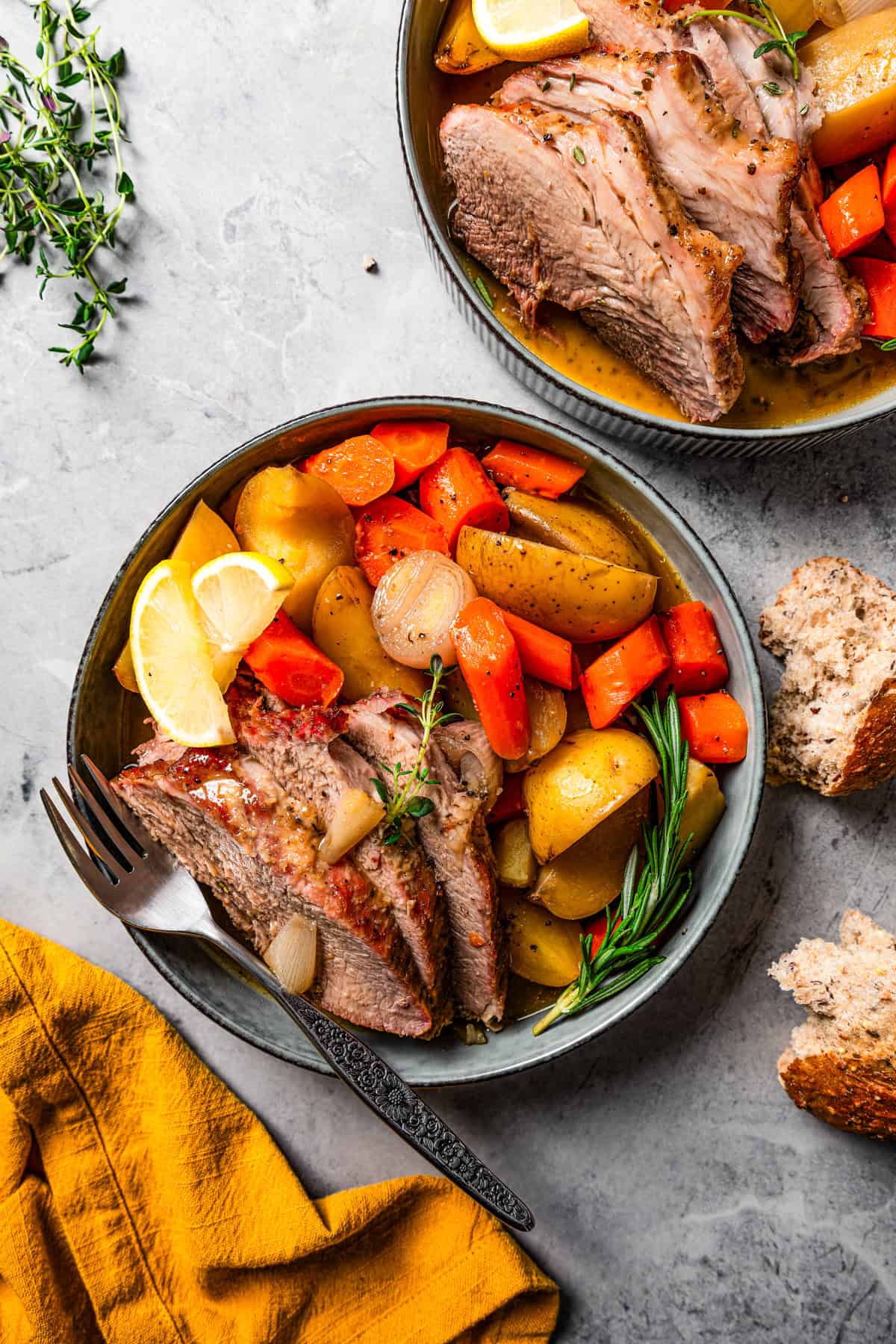 An overhead view shows pork roast slices served with roasted vegetables on a dinner plate, next to a second plate and a yellow cloth napkin.