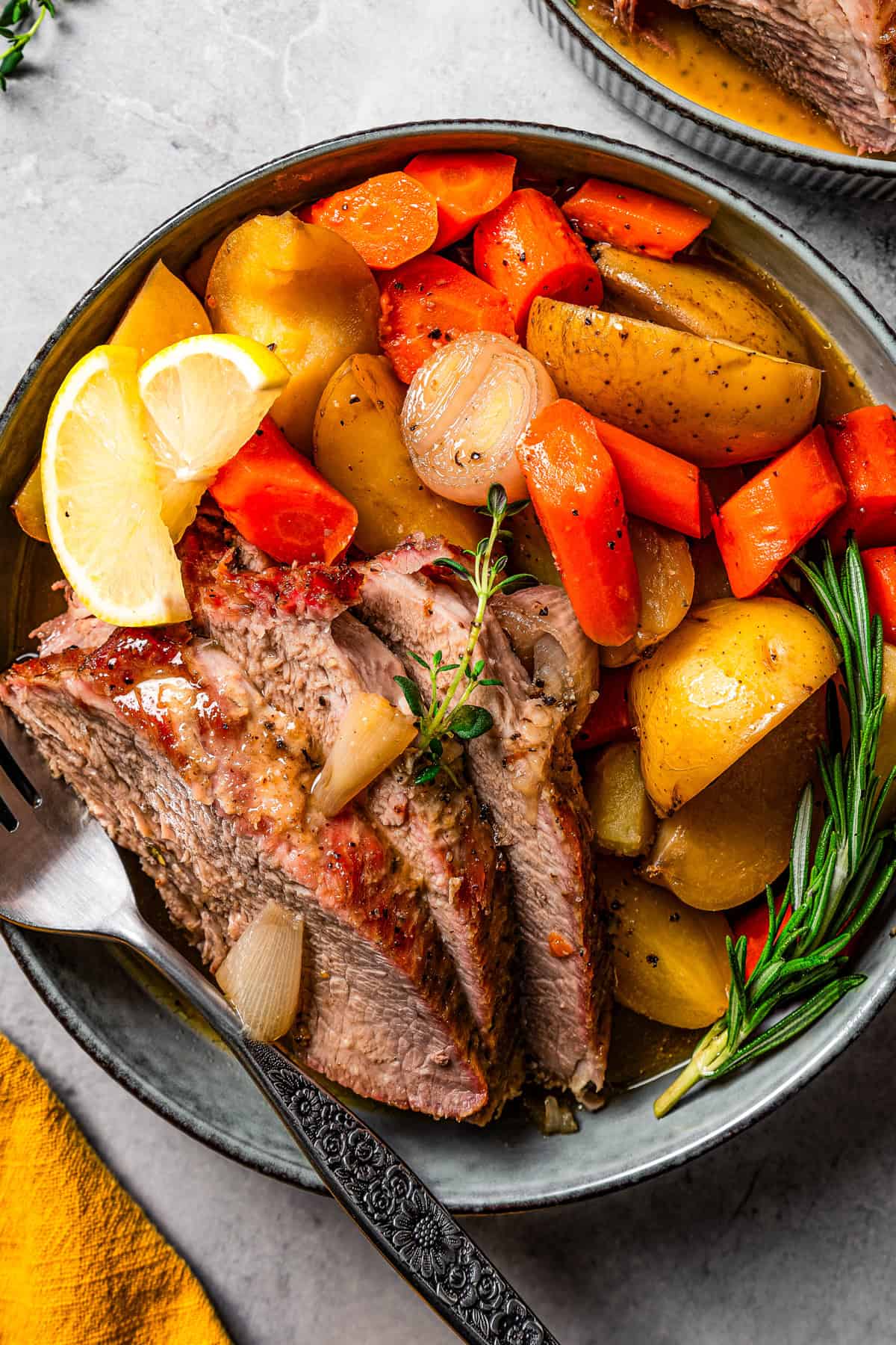 Slices of roasted pork placed next to roasted carrots, potatoes, and shallots, garnished with lemon wedges and served on a stoneware dinner plate.