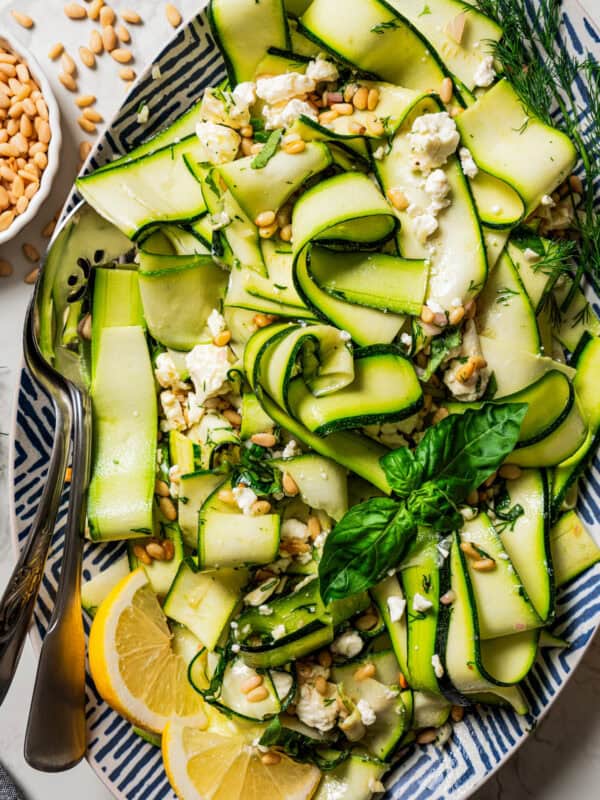 Overhead view of zucchini salad on a large platter garnished with fresh basil leaves and lemon wedges.
