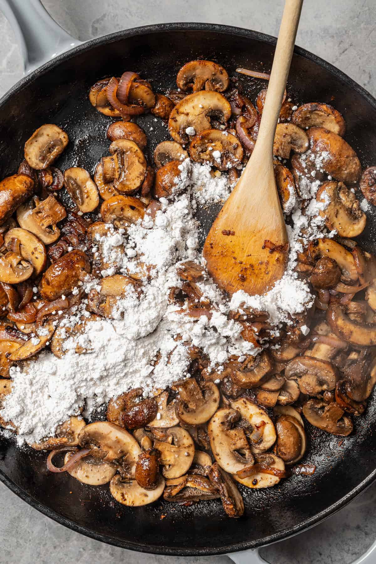 Flour added to sauteed mushrooms and onions in a skillet.