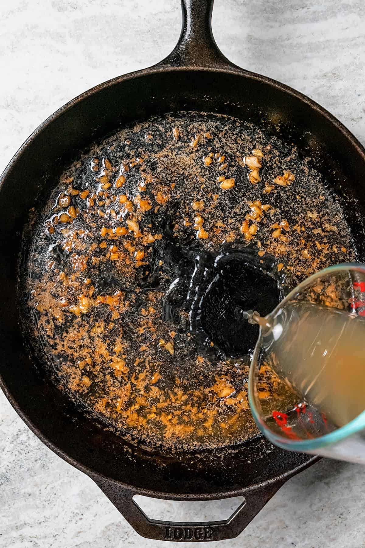 Chicken stock being poured into a skillet to deglaze.