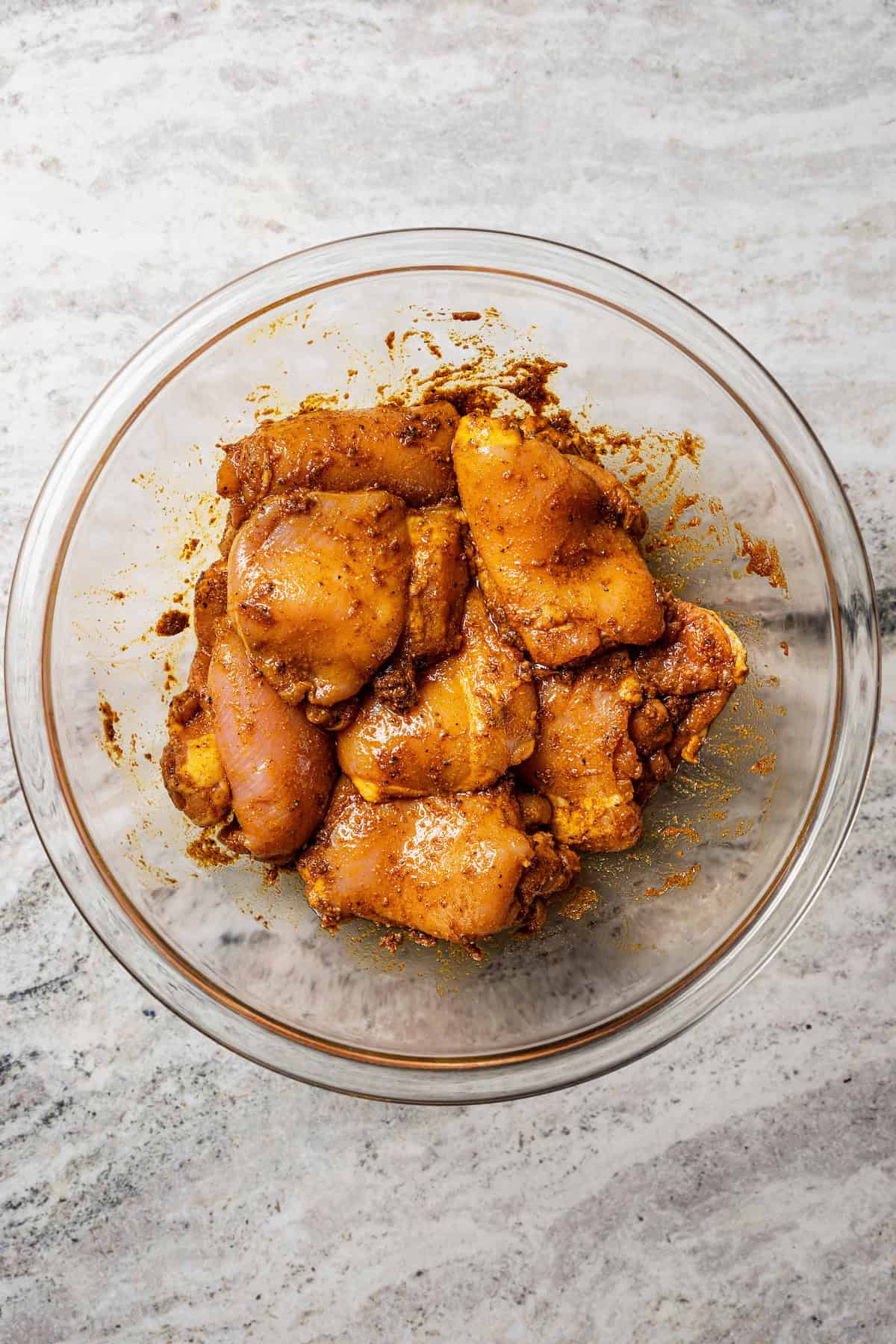 Chicken tossed with shawarma marinade in a glass bowl.