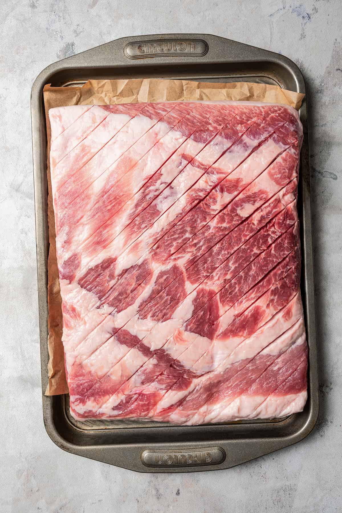 Scored pork belly laid flat over a parchment-lined baking sheet.