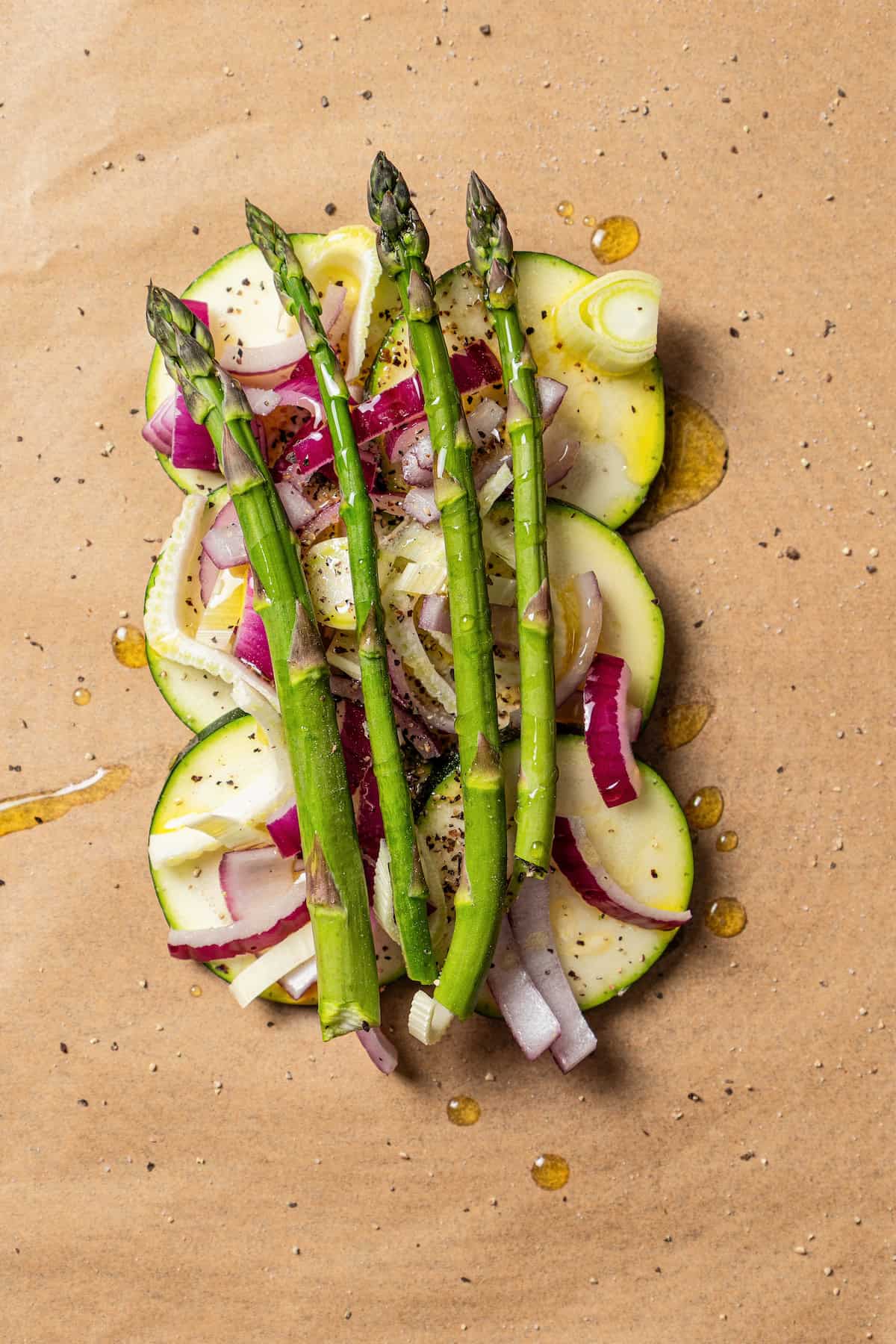 A pile of chopped vegetables topped with asparagus spears on a sheet of parchment paper.