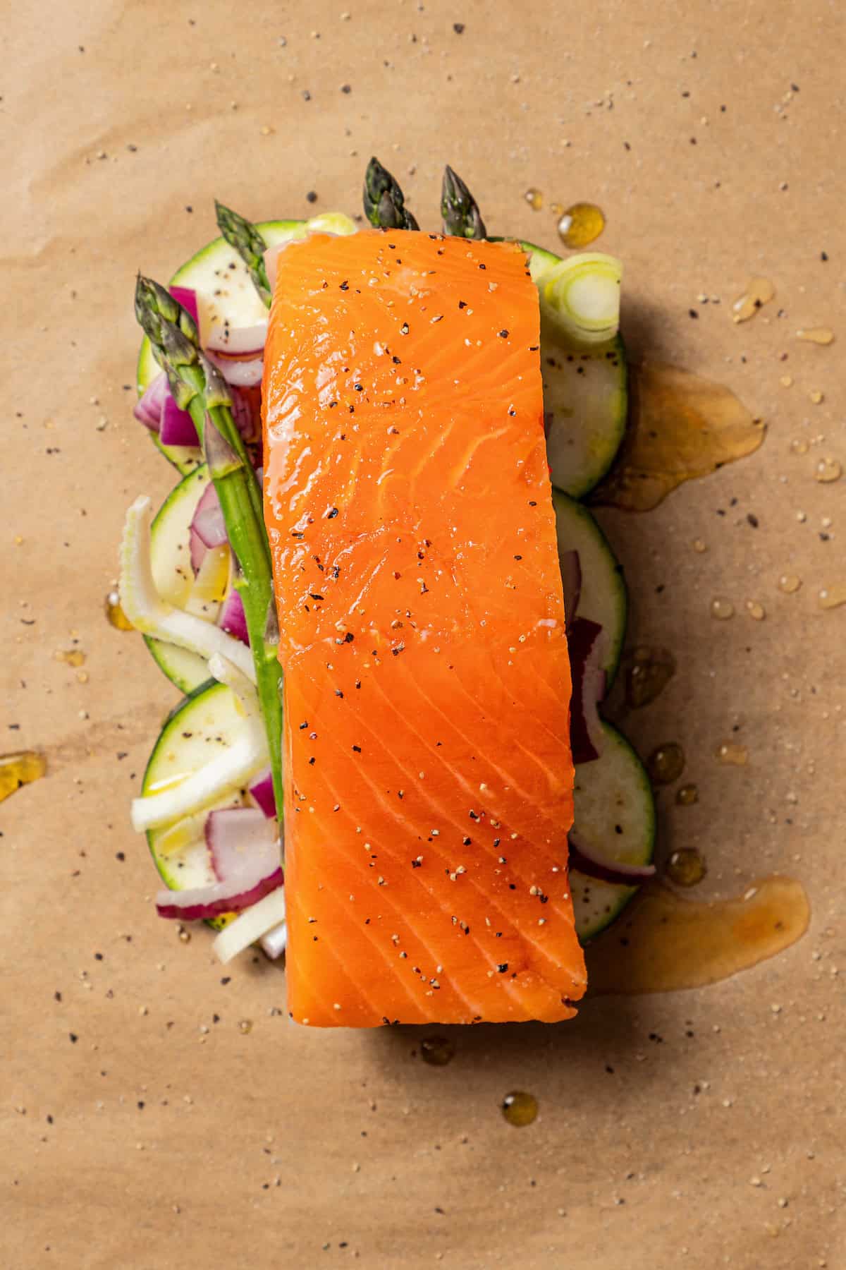 Overhead view of a salmon filet nestled over a bed of chopped vegetables on a sheet of parchment paper.