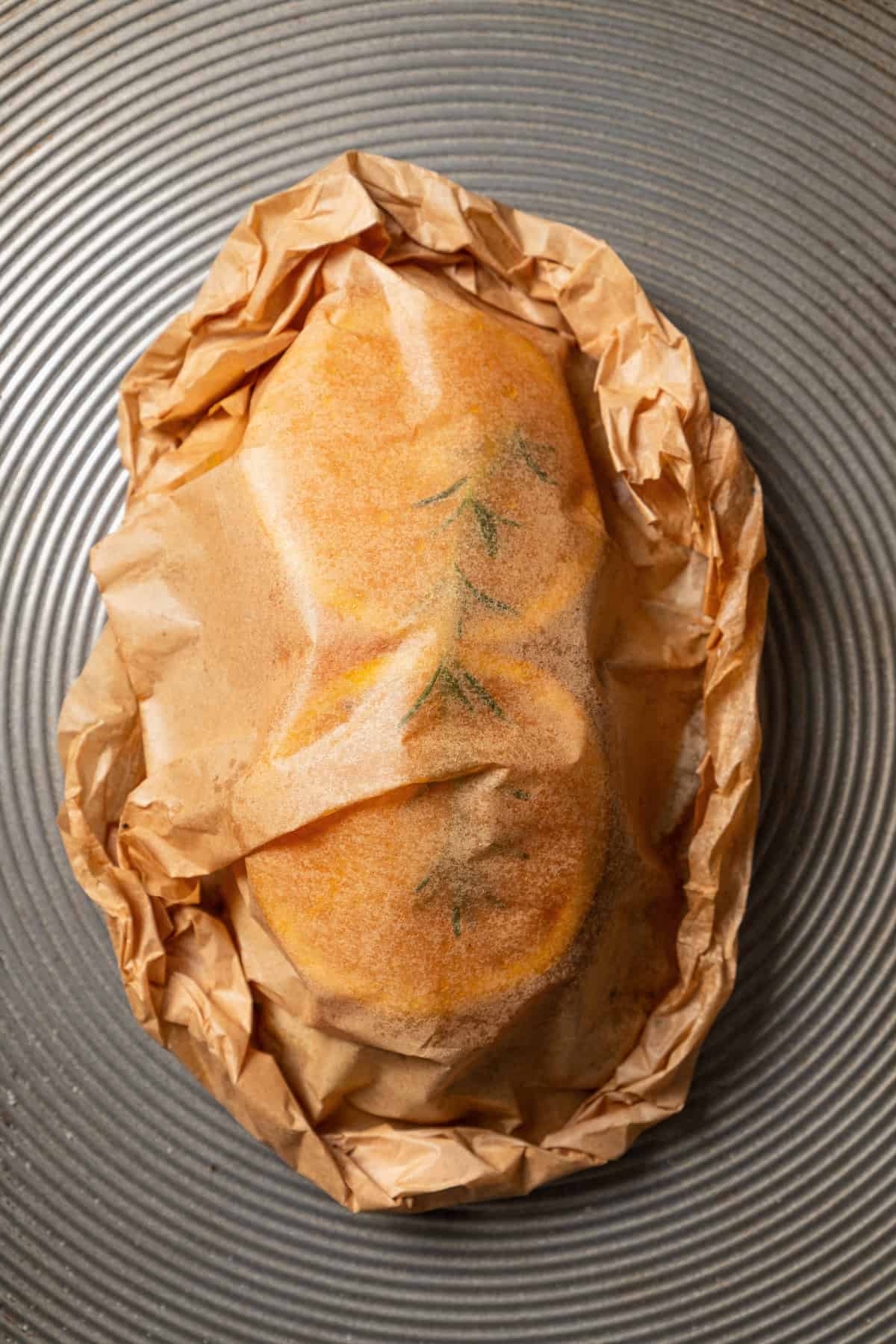 Overhead view of salmon en papillote still wrapped in parchment on a baking sheet.