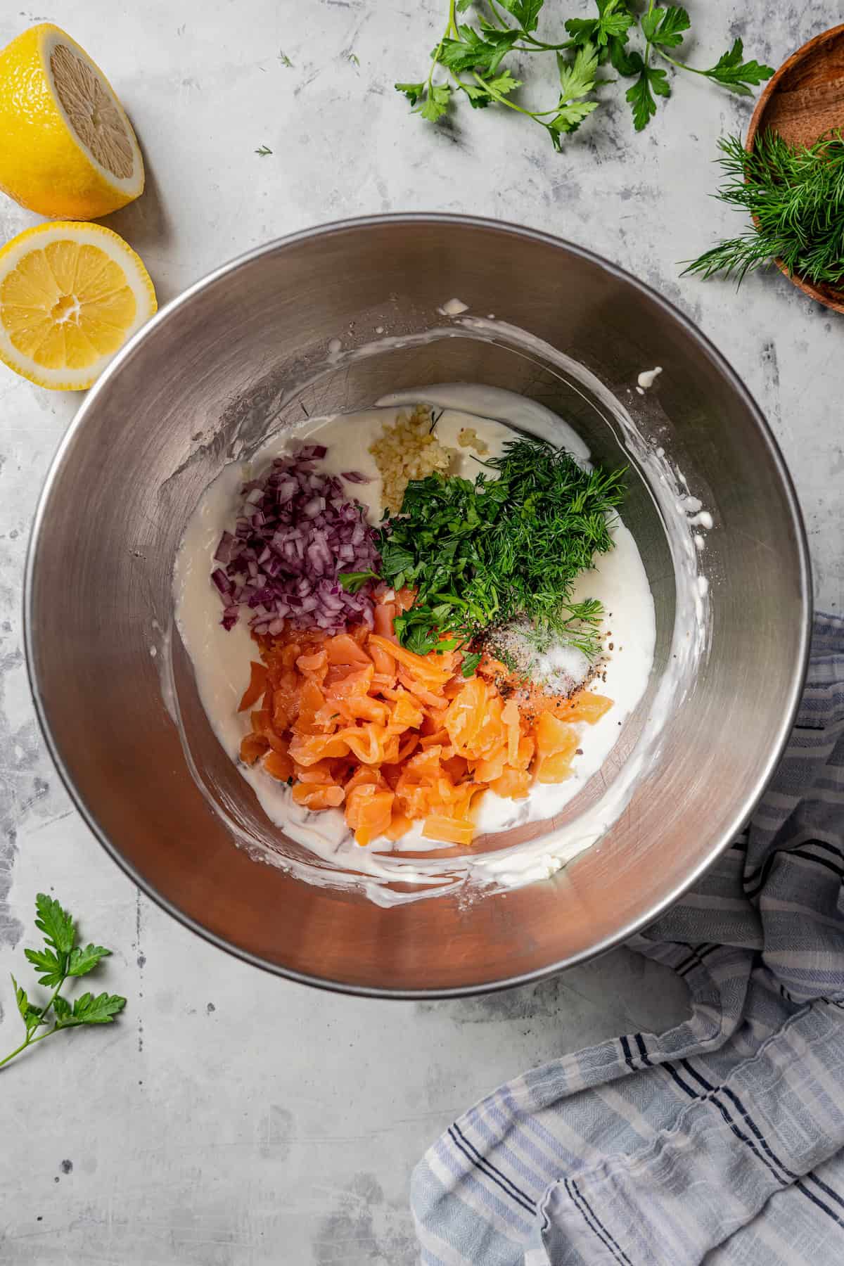 Salmon lox, herbs, and seasonings added to cream cheese dip ingredients in a metal mixing bowl.