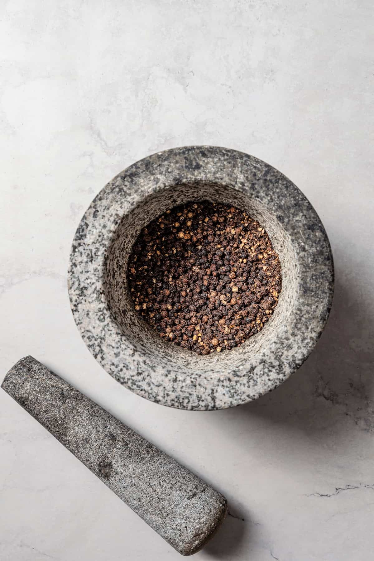 Overhead view of a mortar filled with crushed peppercorns next to a pestle.