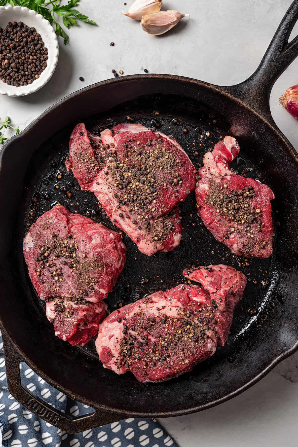 Peppecorn-crusted steaks in a skillet.