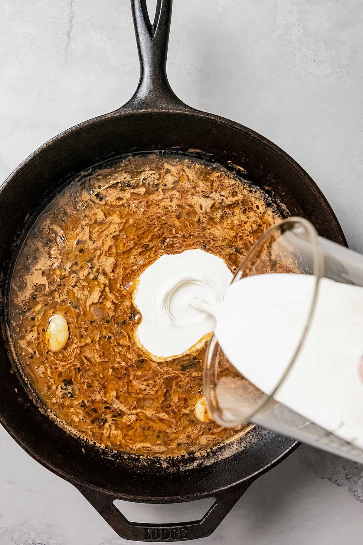 Cream being poured into peppercorn sauce in a skillet.